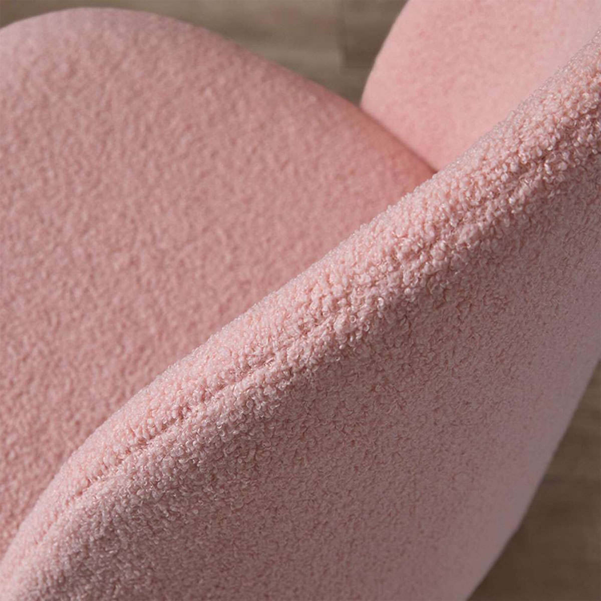 Close-up of a pink textured upholstered chair or sofa corner, showing the fabric weave and curved seat/back edge against a softly blurred neutral background.