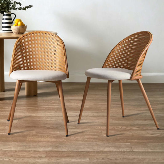 Two modern dining chairs with woven cane backs and light beige upholstered seats, shown on a wood floor in a styled room setting.