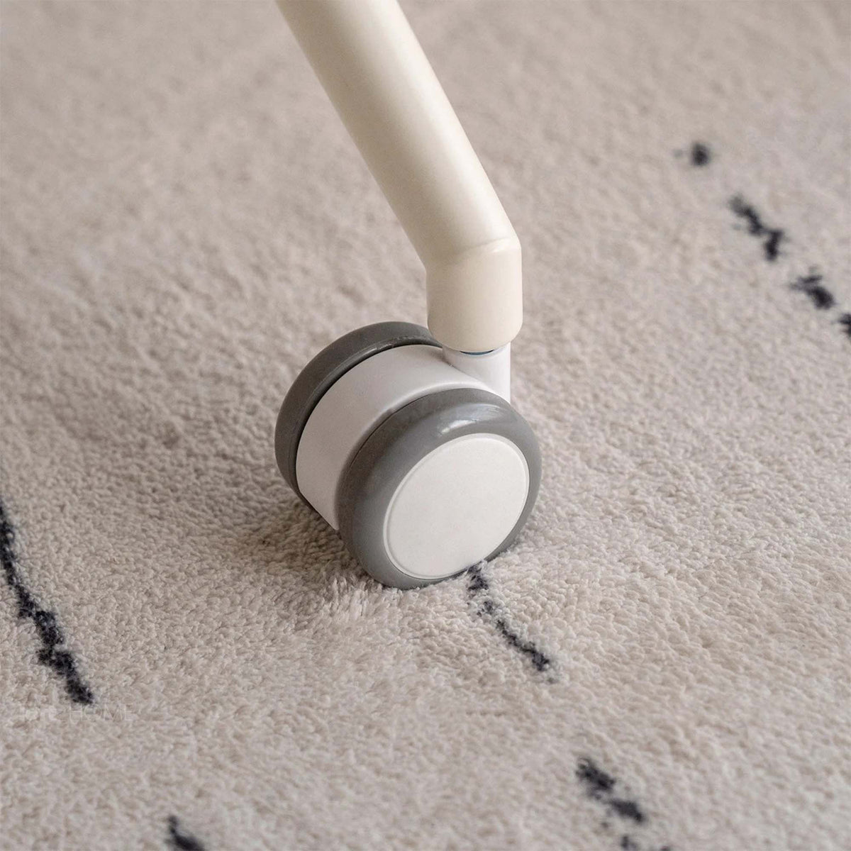 Close-up of a white and gray rolling leg caster on a beige shag rug with black stitched accents.
