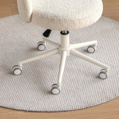 A close-up of a cream-colored, textured boucle office chair with a five-star wheeled base, positioned on a round, light gray woven rug over a light wood floor.
