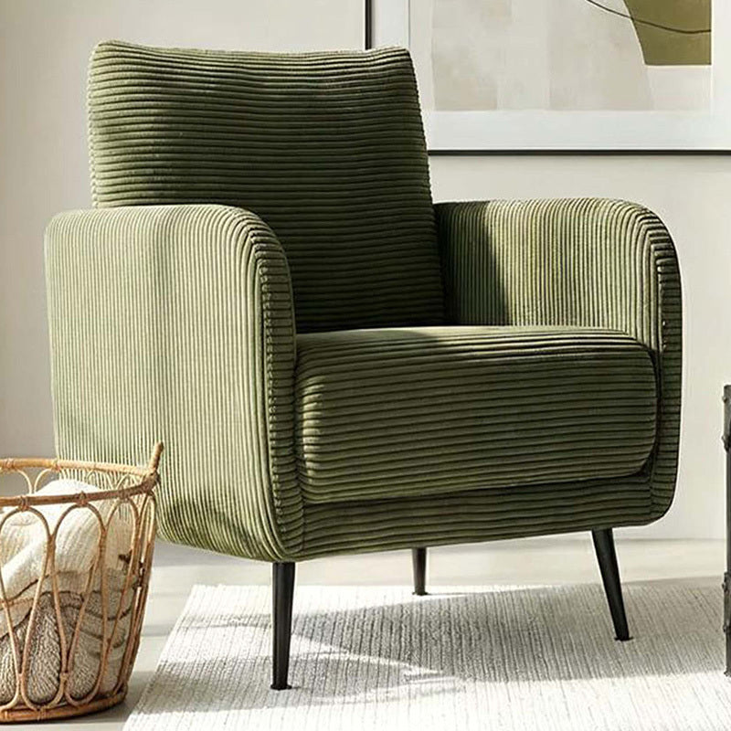 An olive green corduroy armchair with black tapered legs, styled in a modern living room setting next to a woven basket on a light rug.