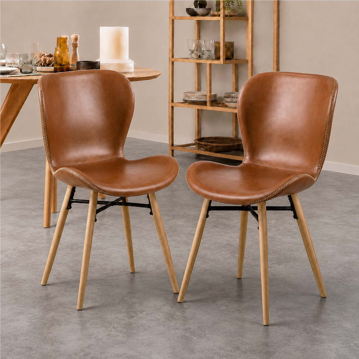 Two modern dining chairs with curved brown leather seats and light natural wood legs, shown in a styled dining room setting.