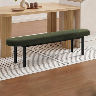 A modern upholstered bench with a dark green cushion and black metal legs, positioned in a styled interior setting with a wooden table, rug, and wood floor.