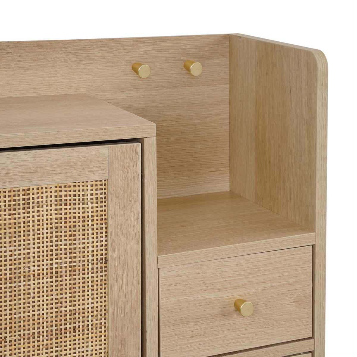 Close-up of a light oak wood cabinet with a woven cane panel door, open shelving, a drawer, and small round brass knobs on a white background.