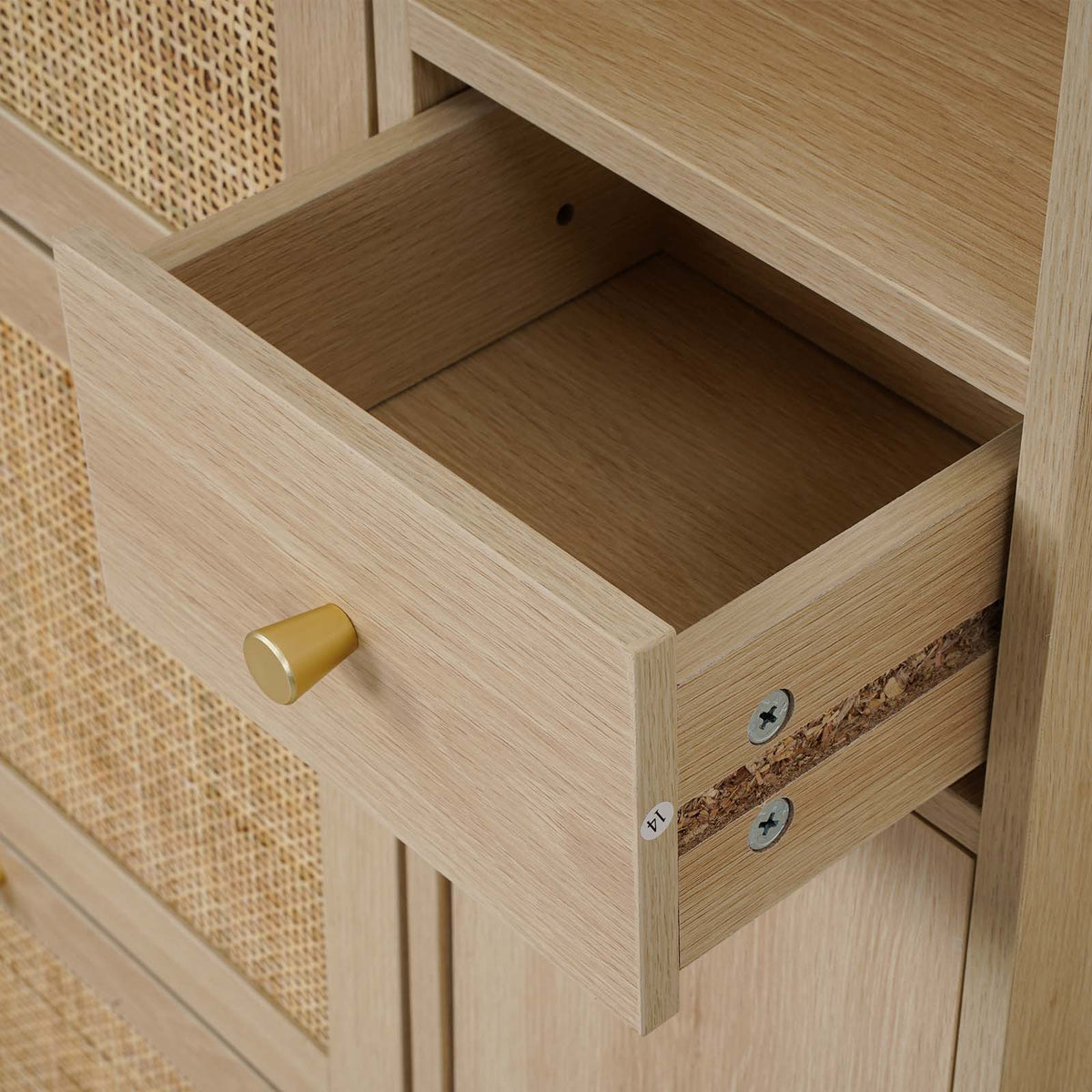 Close-up of a light oak wood cabinet with a drawer pulled open, featuring a round brass pull handle and a woven cane panel on the adjacent door.