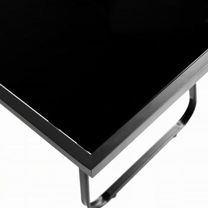 Close-up of a black glossy rectangular tabletop corner with a black metal frame and leg on a white background.