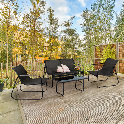 A 4-piece black outdoor patio furniture set including a 3-seat sofa, two armchairs, and a coffee table, arranged on a wooden deck in a backyard setting with trees and a fence.