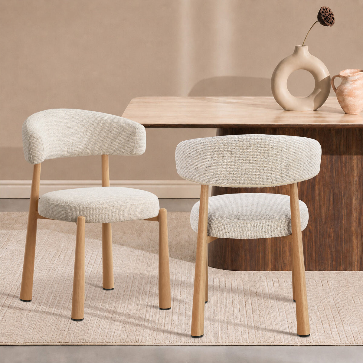 Two upholstered dining chairs with light beige textured fabric and natural wood legs, shown in a styled dining room setting with a wooden table and neutral wall.