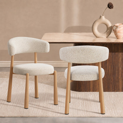 Two upholstered dining chairs with light beige textured fabric and natural wood legs, shown in a styled dining room setting with a wooden table and neutral wall.
